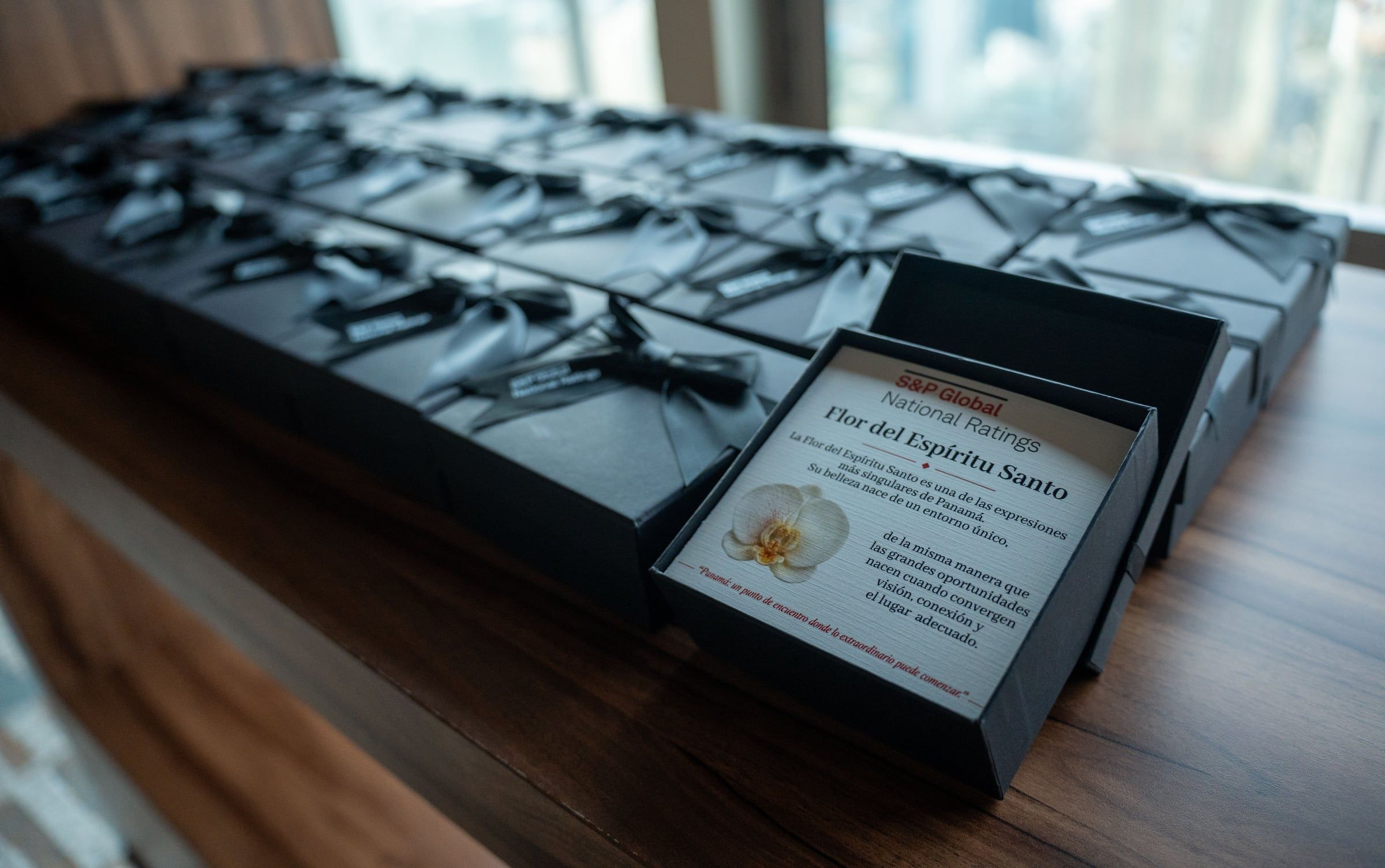Rows of black corporate gift boxes with ribbons and a printed card featuring the Holy Ghost orchid