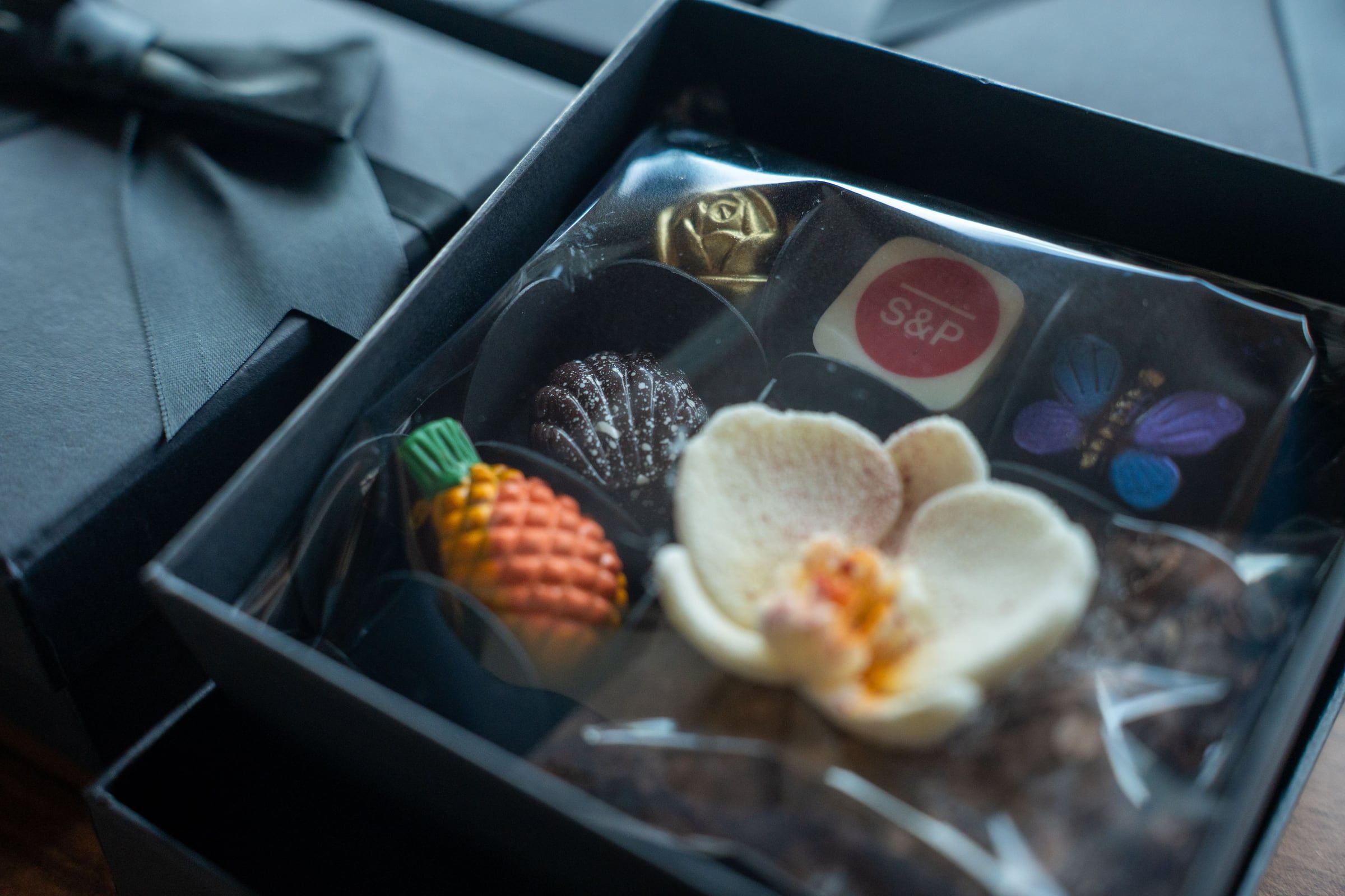 Chocolates artesanales con orquídea, piña y chocolate con logo dentro de una caja negra